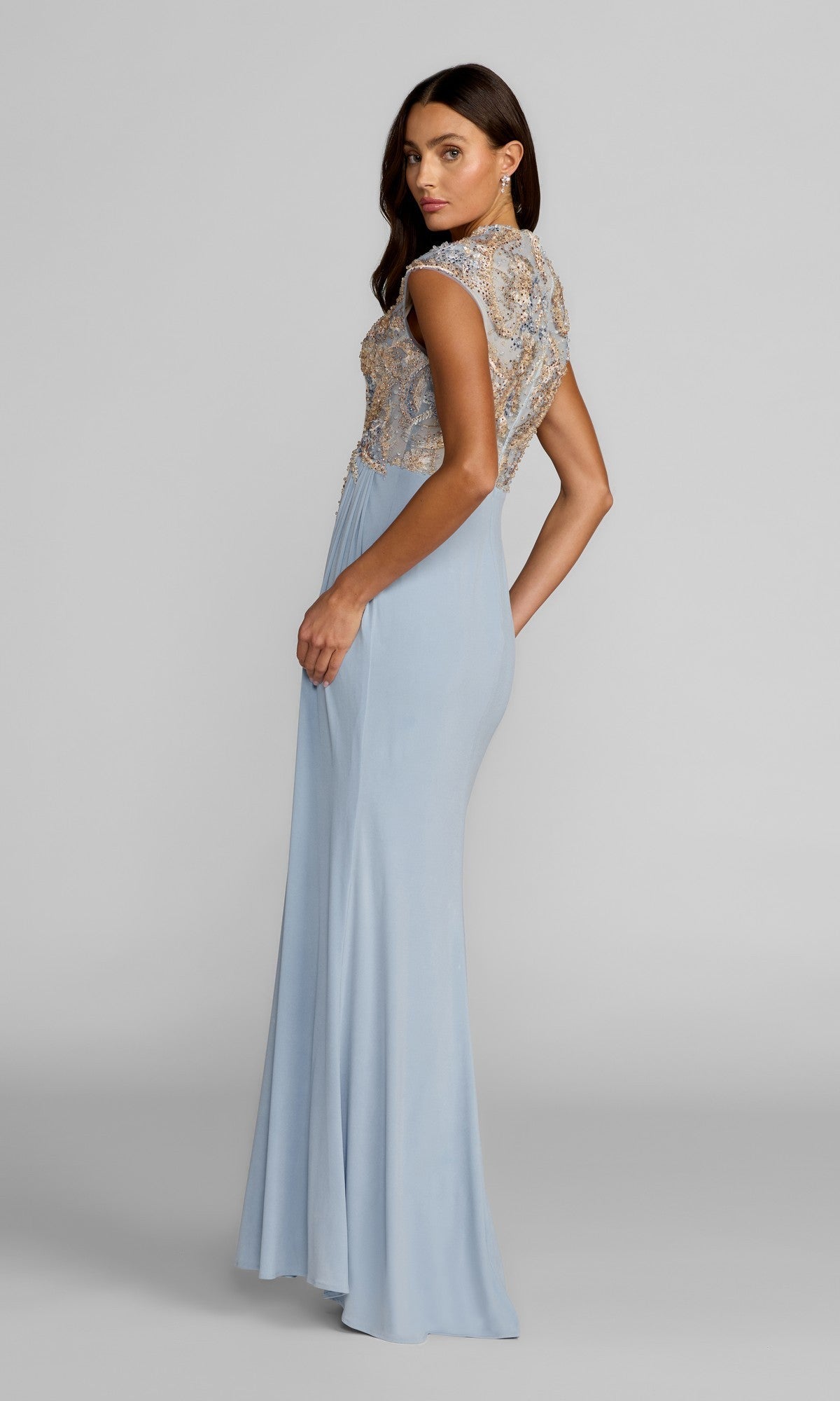 A woman wearing the Long Formal Dress: Mac Duggal 21330—a light blue, floor-length gown featuring intricate beaded detailing and an embroidered bodice with cap sleeves—stands against a plain gray background.